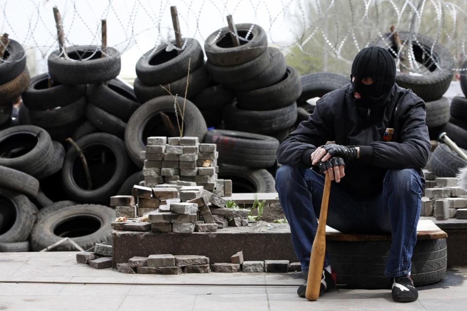 Pro-Russian protester wearing a balaclava and holding a baseball bat sits next to piles of bricks and tyres outside a regional government building in Donetsk