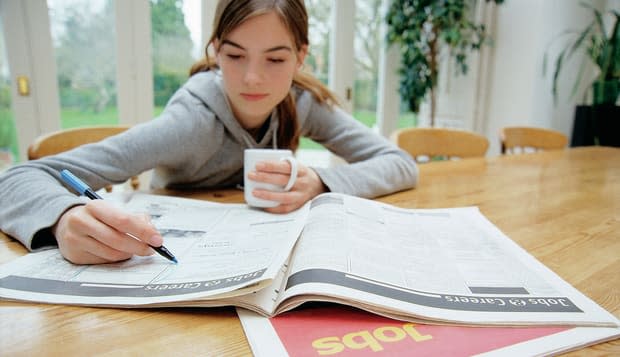Teenage Girl Sitting Behind a Table Searching for Jobs in a Newspaper