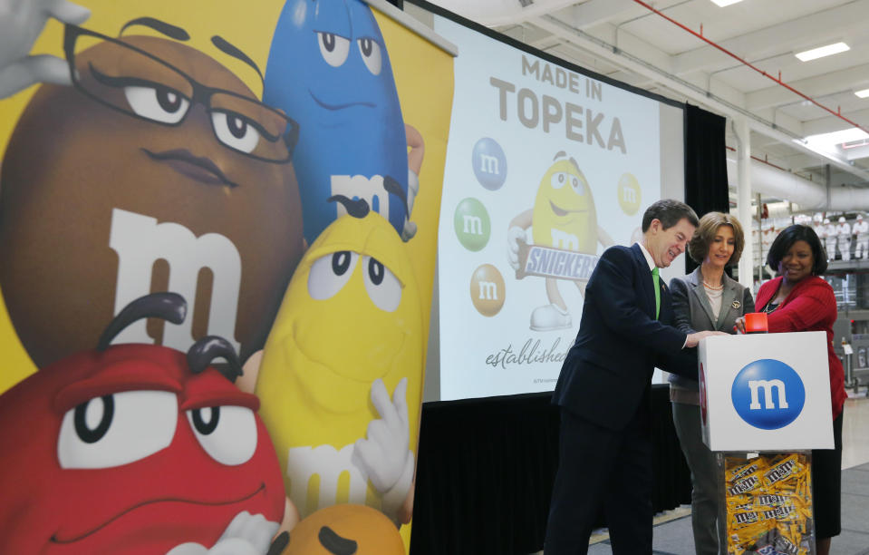 Kansas Gov. Sam Brownback, left, Victoria Mars and Debra Sandler, right, push a button that starts production at the Mars Chocolate North America Topeka Plant near Topeka, Kan., Thursday, March 27, 2014. Victoria Mars is the Chairman of the Board, Mars Inc., and Sandler is president of Mars Chocolate North America. (AP Photo/Orlin Wagner)