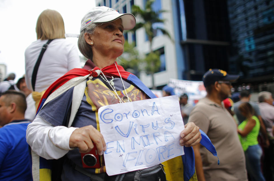 A woman holds a sign that reads in Spanish "Coronavirus is Miraflores," referring to the presidential palace, as she joins the start of an opposition rally in Caracas, Venezuela, Tuesday, March 10, 2020. U.S.-backed Venezuelan political leader Juan Guaido will lead a march aimed at retaking the National Assembly legislative building, which opposition lawmakers have been blocked from entering. (AP Photo/Ariana Cubillos)