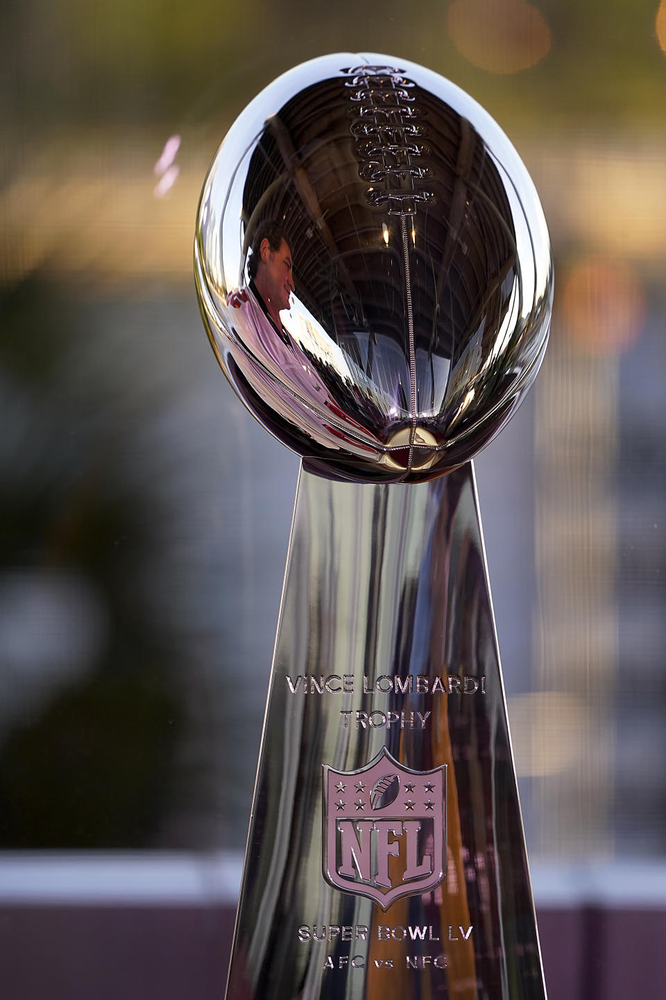 A man is reflected in the Lombardi Trophy at the NFL Experience Thursday, Feb. 4, 2021, in Tampa, Fla. The city is hosting Sunday's Super Bowl football game between the Tampa Bay Buccaneers and the Kansas City Chiefs. (AP Photo/Charlie Riedel)