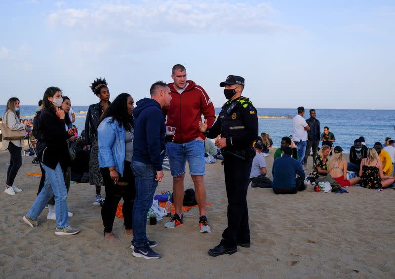 A police office speaks with tourists after vacating a party at Barceloneta beach, in Barcelona