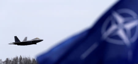 NATO flag flutters as U.S. Air Force F-22 Raptor fighter flies over the military air base in Siauliai, Lithuania, April 27, 2016. REUTERS/Ints Kalnins