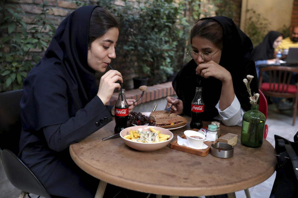 Two Iranians drink Coca-Cola at a cafe in downtown Tehran, Iran, Wednesday, July 10, 2019. Whether at upscale restaurants or corner stores, American brands like Coca-Cola and Pepsi can be seen throughout Iran despite the heightened tensions between the two countries. U.S. sanctions have taken a heavy toll, but Western food, movies, music and clothing are still widely available. (AP Photo/Ebrahim Noroozi)