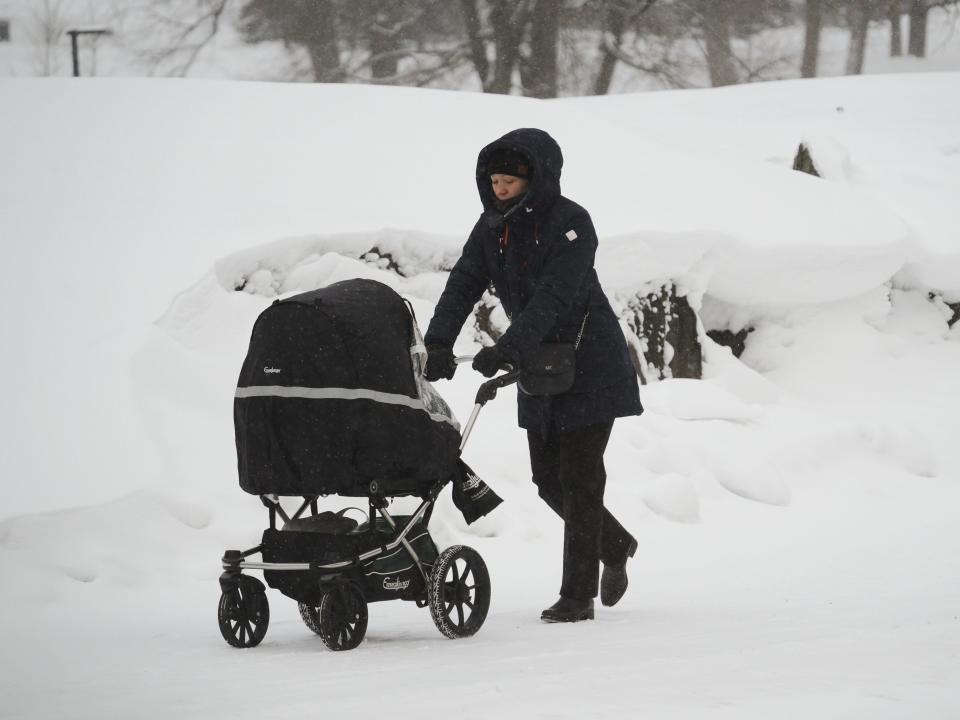 A woman pushes a baby in a stroller through the snow in Helsinki.