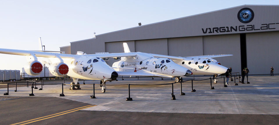 FILE - In this Sept. 25, 2013, file photo, the first SpaceShipTwo is seen suspended at center beneath its twin-fuselage mother ship at the Virgin Galactic hangar at Mojave Air and Space Port in Mojave, Calif. Boeing plans to invest $20 million in Virgin Galactic as the space tourism company nears its goal of launching passengers on suborbital flights. The companies announced the investment Tuesday, Oct. 8, 2019, saying they will work together on broadening commercial access to space and transforming global travel technologies. Virgin Galactic has conducted successful test flights of its winged rocket ship at Mojave, California, and is preparing to begin operations at Spaceport America in New Mexico. (AP Photo/Reed Saxon, File)