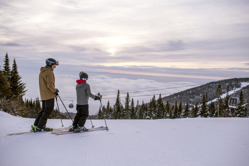 Father and child skiing at Le Massif de Charlevoix in Quebec, pausing at the top of the run to enjoy the view