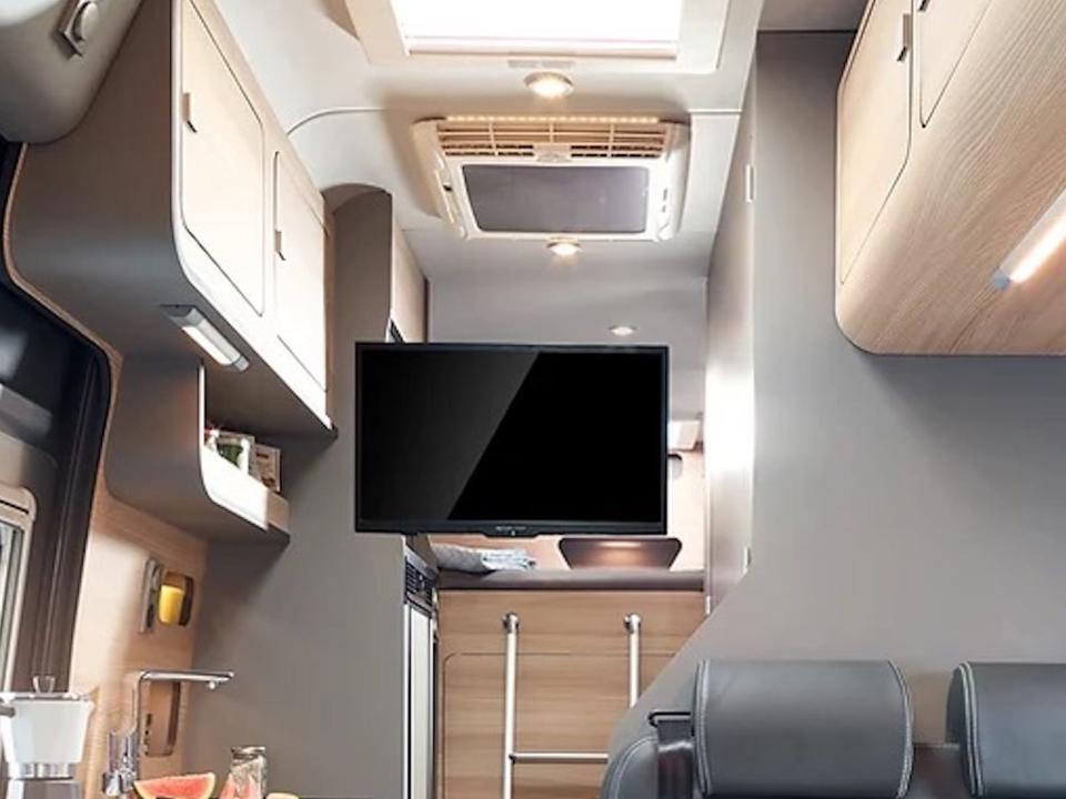 A living room near a kitchen in the camper van. The TV is swiveled out.