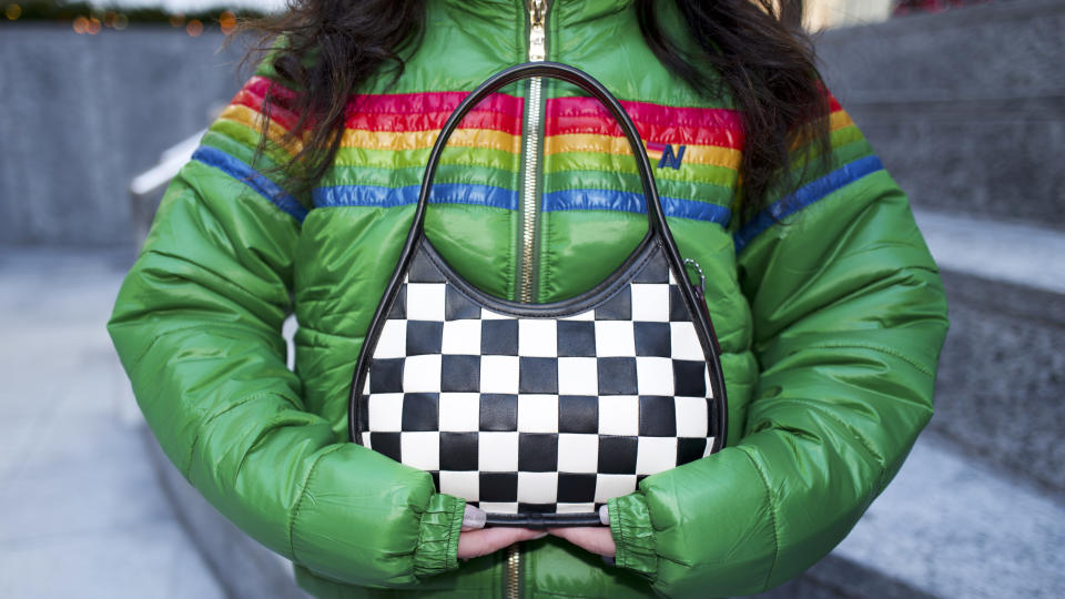 woman in green jacket holding a black and white checkered coach bag 