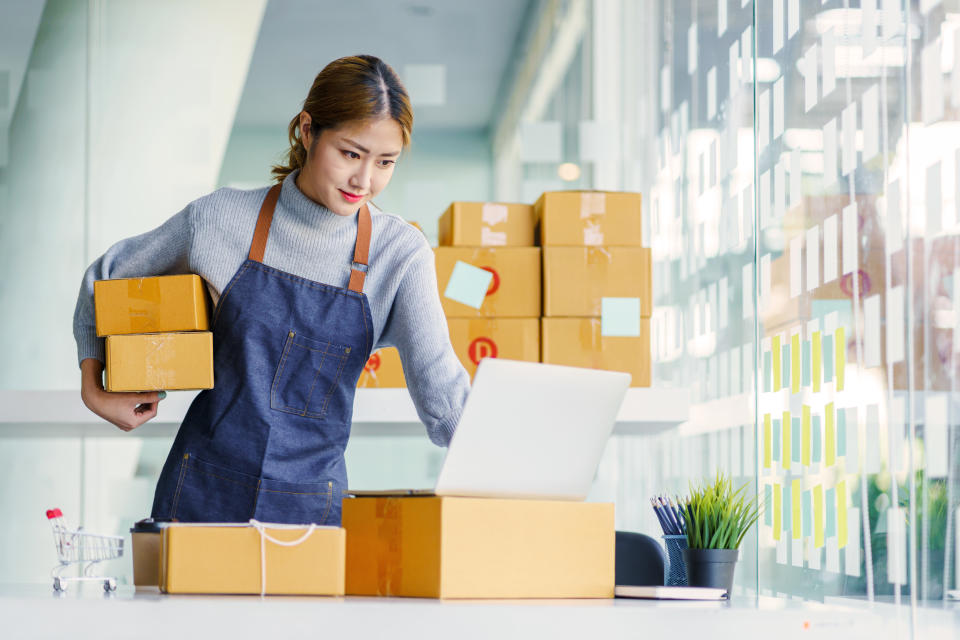 Young Asian female Small Business SME entrepreneur checking email order in laptop with box for packaging.