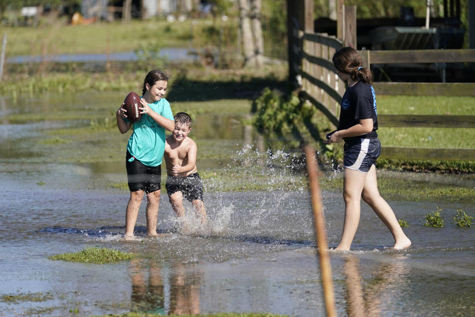 Siblings Chancy, left, Blayke, center, and Alayna Trahan, play in a field that was flooded from Hurricane Delta, at their home in Hayes, La., Saturday, Oct. 10, 2020. (AP Photo/Gerald Herbert)