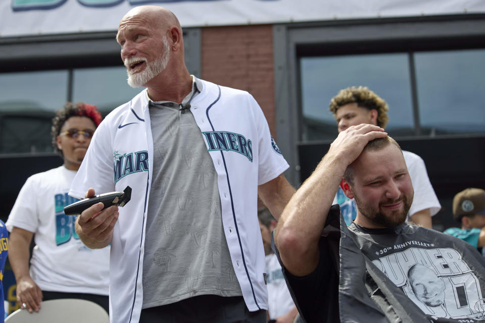 Former Seattle Mariners player Jay Buhner turns and jokes with the crowd as he shaves catcher Cal Raleigh's head on Buhner Buzz Night, Thursday, June 13, 2024, in Seattle. The promotion is based on Buhner's shaved-head style. (AP Photo/John Froschauer)