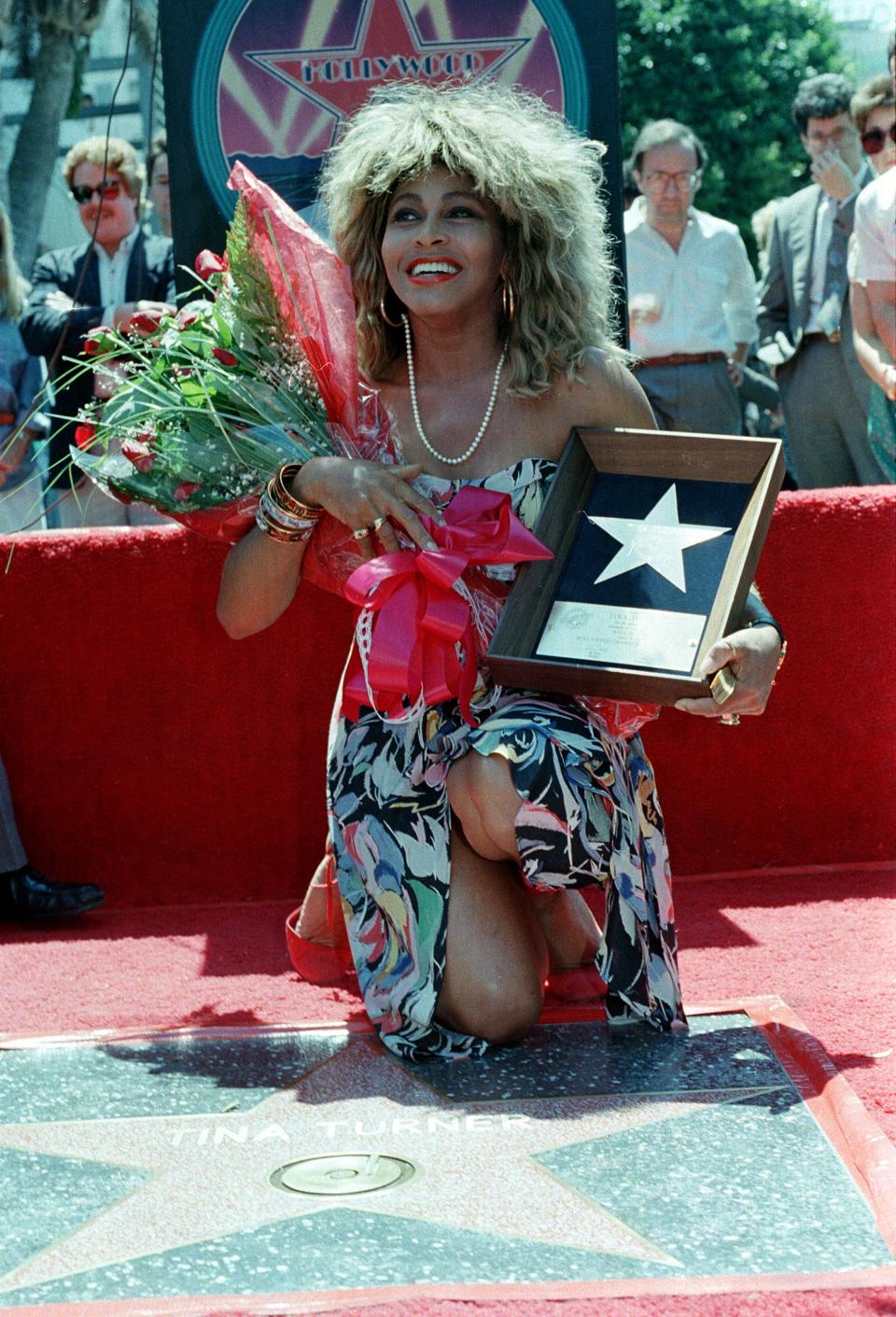 Rock and roll singer Tina Turner poses with her plaque and a bouquet of roses near her star on the Hollywood Walk of Fame during the unveiling ceremony in Los Angeles, Ca., Aug. 28, 1986.