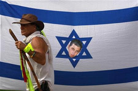 An Israeli activist walks past a national flag with the face of captured soldier Gilad Shalit pasted on it during a protest calling for his release, at Kibbutz Degania Alef