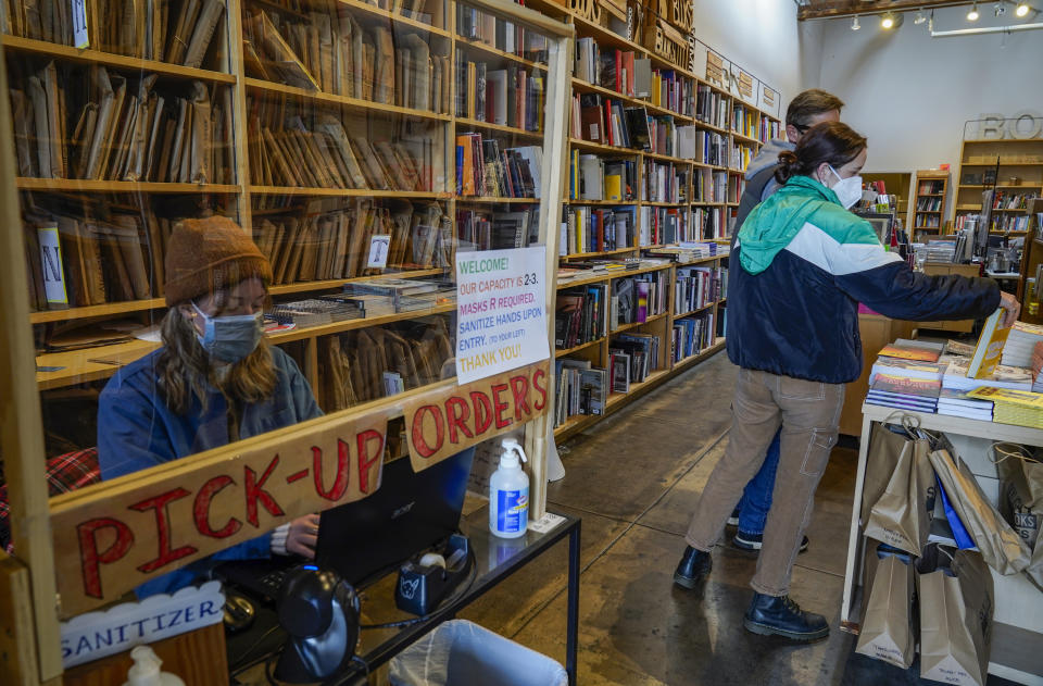 Hannah Martin works behind a plexiglass sheet, as she delivers book pickup orders at the Skylight Book store in the Los Feliz neighborhood of Los Angeles Monday, Jan. 25, 2021. California has lifted regional stay-at-home orders statewide in response to improving coronavirus conditions. Public health officials said Monday that the state will return to a system of county-by-county restrictions intended to stem the spread of the virus. Local officials could choose to continue stricter rules. The state is also lifting a 10 p.m. to 5 a.m. curfew. (AP Photo/Damian Dovarganes)