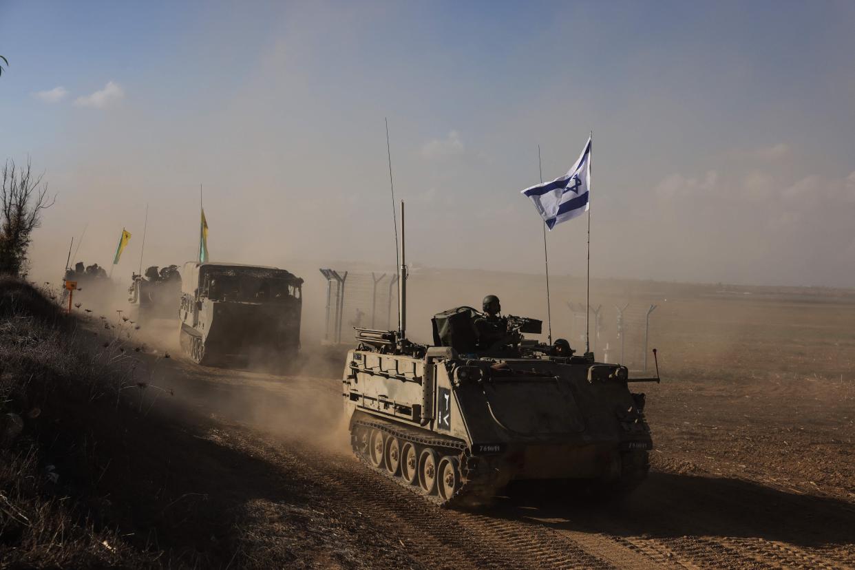 Tanks filing in the desert, the lead one flying an Israeli flag, kicking up dust under a bright blue sky.