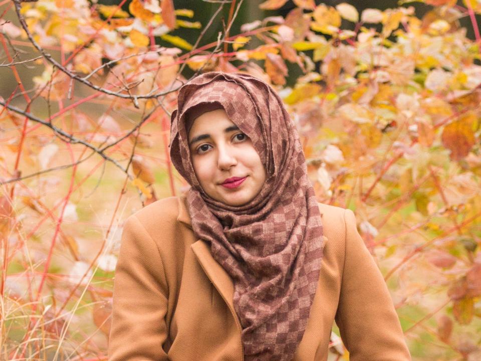 Anmol Irfan smiling and sitting outside on a rock. It's fall, and there are orange leaves.