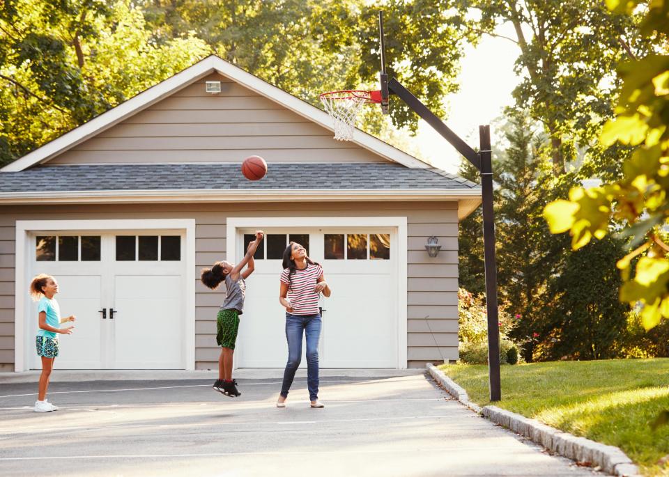 Mother and children playing basketball on driveway.