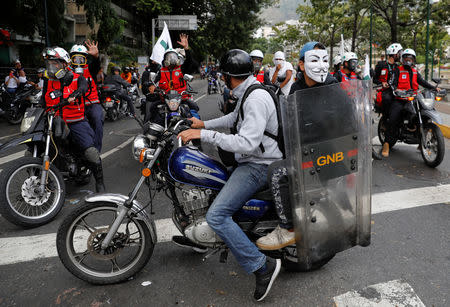 A protester wearing a Guy Fawkes mask holds a shield of National Guard during a protest of opposition supporters against Venezuelan President Nicolas Maduro's government in Caracas, Venezuela January 23, 2019. REUTERS/Manaure Quintero