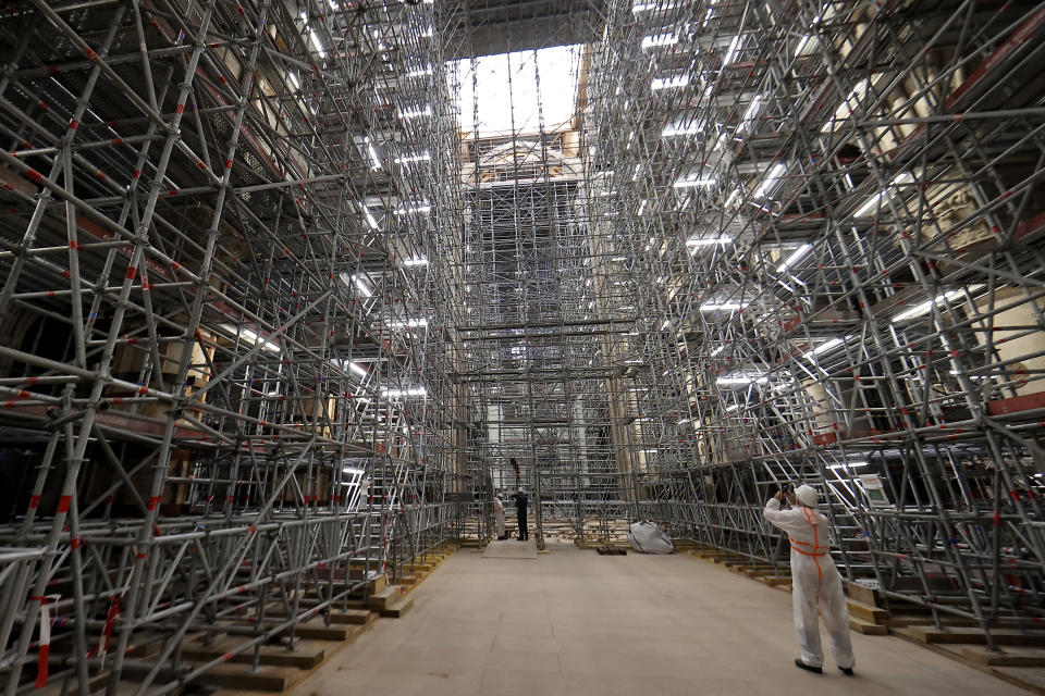 FILE - A worker takes a picture of the scaffolding's at the reconstruction site ahead a visit of the French President at the Notre-Dame de Paris Cathedral, in Paris, Friday, April 15, 2022. France's Notre Dame Cathedral's reconstruction is progressing enough to allow its reopening to visitors and masses at the end of next year, less than six years after the after the shocking fire that tore through its roof, French officials said as an exhibit pays tribute to hundreds of artisans working on it. (Ian Langsdon, Pool via AP, File)