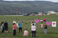 Canadian Forces Snowbirds planes are seen in the background as people place hearts and signs on the fence surrounding the airport in Kamloops, Canada, Sunday, May 17, 2020. A Canadian aerobatic jet crashed into the British Columbia neighborhood of Kamloops on Sunday during a flyover intended to boost morale during the pandemic, killing one crew member, seriously injuring another and setting a house on fire. (Jonathan Hayward/The Canadian Press via AP)