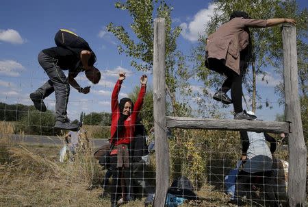 Migrants jump over a road protection fence as they leave a collection point in the village of Roszke, Hungary September 9, 2015. REUTERS/Marko Djurica