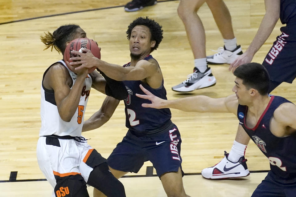 Liberty's Darius McGhee (2) fouls Oklahoma State guard Rondel Walker (5) as Blake Preston also defends in a first-round NCAA tournament game. (AP Photo/Charles Rex Arbogast)