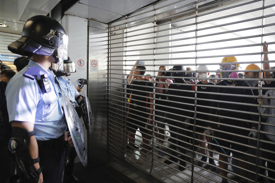 Police watch demonstrators through a closed entrance gate at the Kwun Tong MTR station in Hong Kong, Saturday, Aug. 24, 2019. Chinese police said Saturday they released an employee at the British Consulate in Hong Kong as the city's pro-democracy protesters took to the streets again, this time to call for the removal of "smart lampposts" that raised fears of stepped-up surveillance. (AP Photo/Kin Cheung)