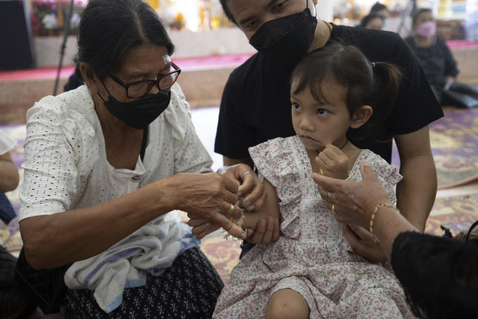 Relatives of the victims of the mass killing attack tie holy threads on the wrists of 3 year old Paweenuch Supolwong, the only child to emerge unscathed, inside Wat Rat Samakee temple in Uthai Sawan, north eastern Thailand, Saturday, Oct. 8, 2022. A former police officer burst into a day care center in northeastern Thailand on Thursday, killing dozens of preschoolers and teachers before shooting more people as he fled. (AP Photo/Wason Wanichakorn)