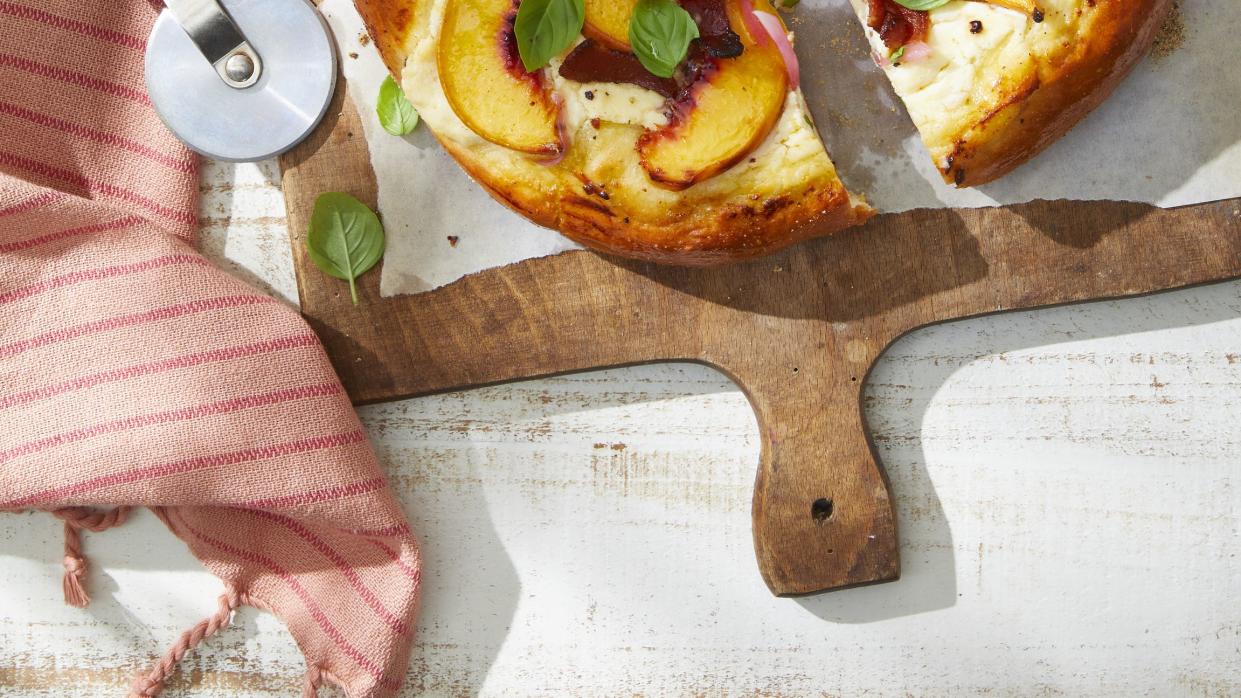 a peach and bacon pizza with basil on a cutting board