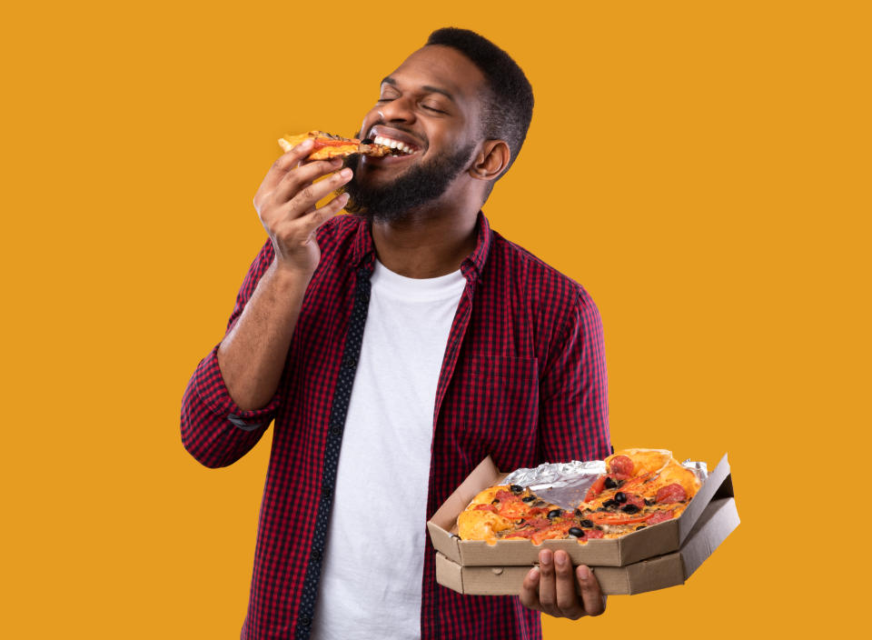 <p>Happy African Young Man Enjoying Pizza Biting Tasty Slice Posing With Box Over Yellow Background. Junk Food Lover Eating Italian Pizza In Studio. Unhealthy Male Nutrition And Cheat Meal</p> 