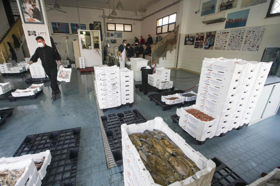 Buyers, in background, respect safety distance and wear protective mask during an auction in a wholesale fish market, in Fiumicino, Monday, March 30, 2020. Italy’s fishermen still go out to sea at night, but not as frequently in recent weeks since demand is down amid the country's devastating coronavirus outbreak. (AP Photo/Andrew Medichini)