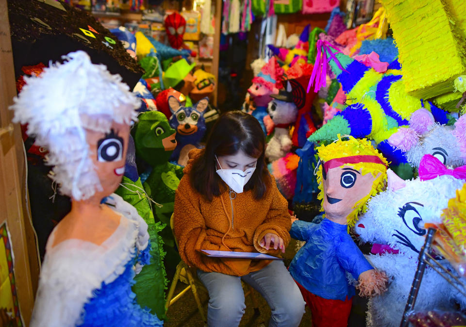 Sarita Reyes works on her school assignments on an iPad at her mother's shop, Pinata Time, on Tuesday, Dec. 15, 2020, in San Antonio, Texas. With Fiesta canceled, children’s birthday parties called off and government officials pleading with residents to stay home during normally festive holidays, the pandemic presented a noxious brew for “piñateros” in town. (Billy Calzada/The San Antonio Express-News via AP)