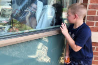 Six-year-old Brody Barker waves to his father, Daryl, from outside his hospital room on Monday, July 26, 2021, in Osage Beach, Mo. Brody and his mother, Billie, have spent nearly three weeks camped outside Lake Regional Hospital's Intensive Care Unit as Barker recovers from COVID-19. "I think that him being able to see us made him fight more," she said. (AP Photo/Sarah Blake Morgan)