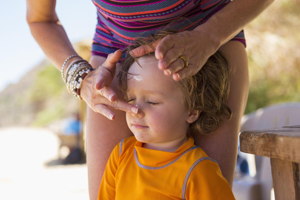 mom in swimsuit applying sunscreen to child's forehead and nose in swim t-shirt