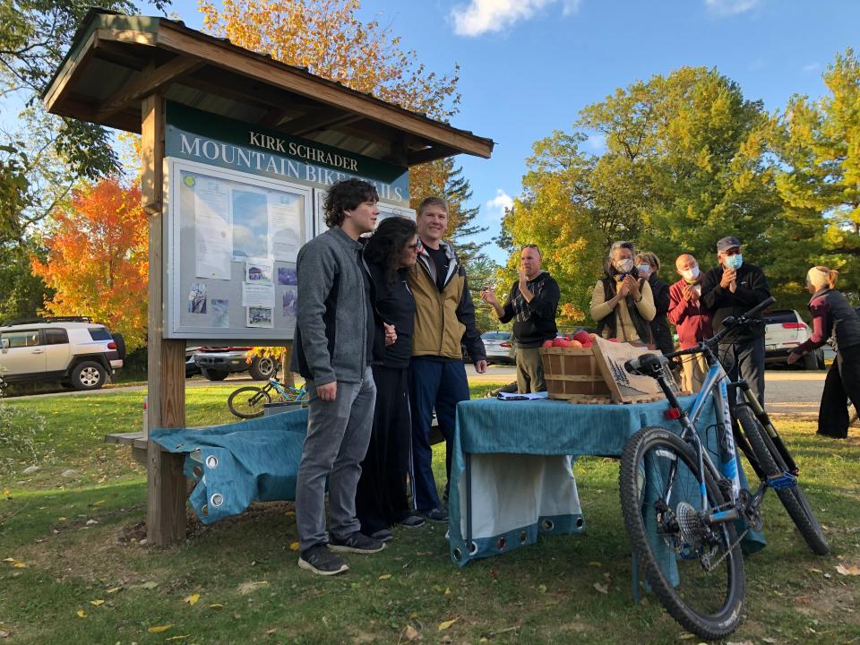 Janet Moore Schrader and her sons, Nick, left, and Alex, gather in front of the trail kiosk Sept. 30 after renaming the mountain bike trails in honor of their late husband and father, Kirk Schrader, at Chikaming Township Park and Preserve. Kirk’s bike rests on the table.