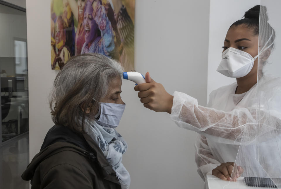 In this Wednesday, May 13, 2020 photo, a masked unidentified patient has her temperature checked by dental assistant Margot Daussat prior to a dental appointment at a dental office in Paris. Those with toothache that suffered through France's two-month lockdown, finally have hope to end the pain. Dental practices are cautiously re-opening and non-emergency dentist appointments are now permitted around the country, as the French government eased confinement restrictions from Monday. (AP Photo/Michel Euler)