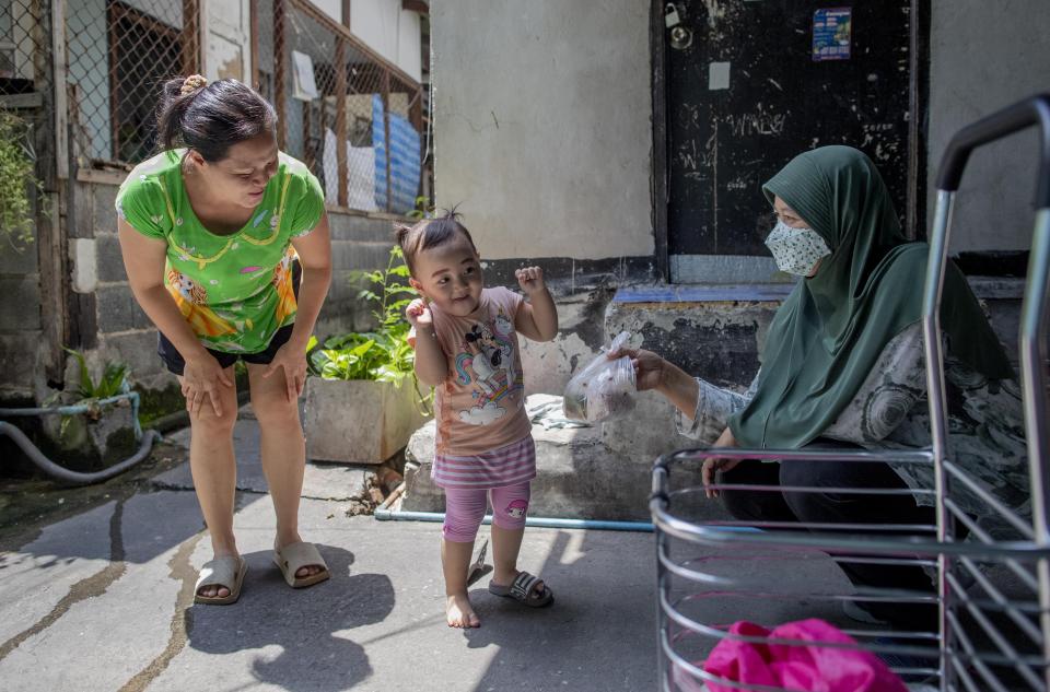 Numcha Then, a three-year old child of a migrant Myanmar parents, reacts to her teacher Sure Etsy Tianmanee as she receives a meal in Bangkok, Thailand, Wednesday, June 24, 2020. During the third month that schools remained closed due to the coronavirus outbreak, teachers have cooked meals, assembled food parcels and distributed them to families in this community sandwiched between an old railway line and a khlong, one of Bangkok’s urban canals. (AP Photo/Gemunu Amarasinghe)