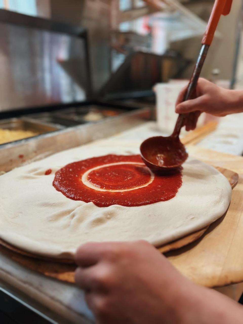 A Big Jay's Pizzeria employee spreads sauce on pizza dough.