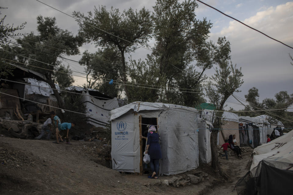 In this Friday Oct. 4, 2019 photo, a woman enters a tent in a makeshift refugee and migrant camp on the fringes of the overcrowded Moria camp on the Greek island of Lesbos. Greece's conservative government announced Wednesday Nov. 20, 2019, plans to overhaul the country's migration management system, and replacing existing camps on the islands with detention facilities and moving and 20,000 asylum seekers to the mainland over the next few weeks. (AP Photo/Petros Giannakouris)