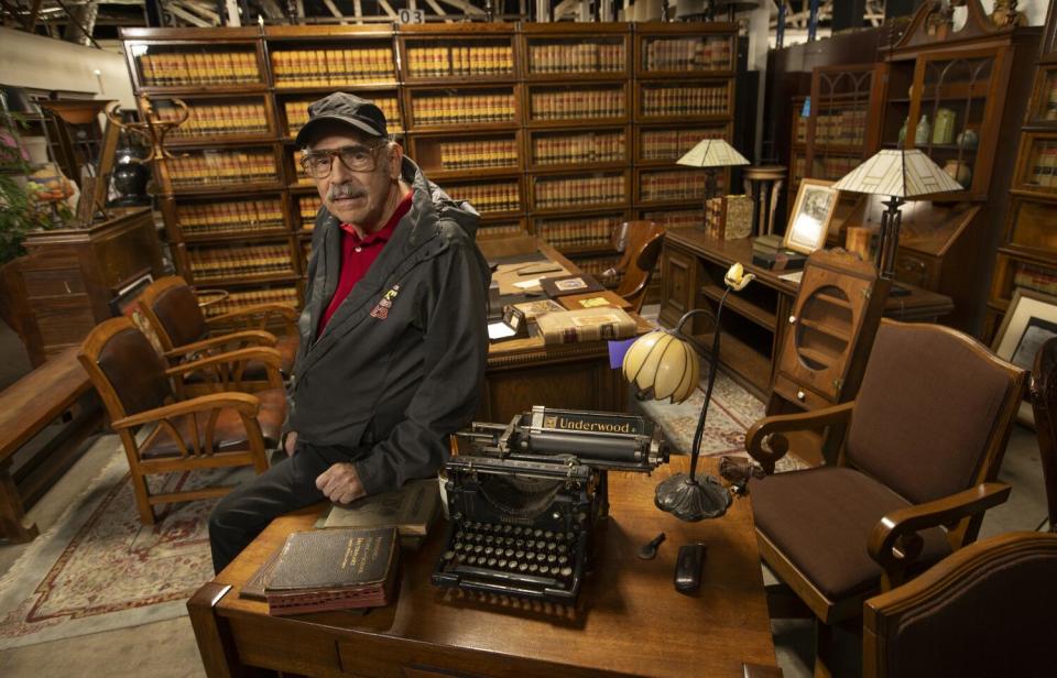 A man sits on a desk with a typewriter and books.