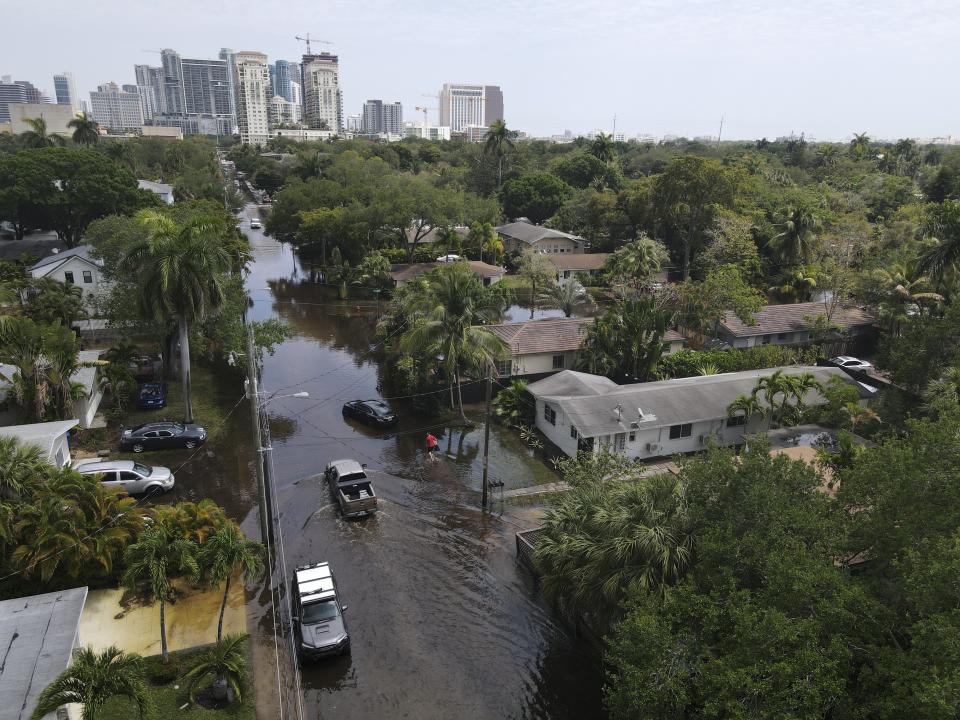 FILE - Trucks and a resident on foot make their way through receding floodwaters in the Sailboat Bend neighborhood of Fort Lauderdale, Fla., April 13, 2023. Over 25 inches of rain fell in South Florida since Monday, causing widespread flooding. (AP Photo/Rebecca Blackwell, File)