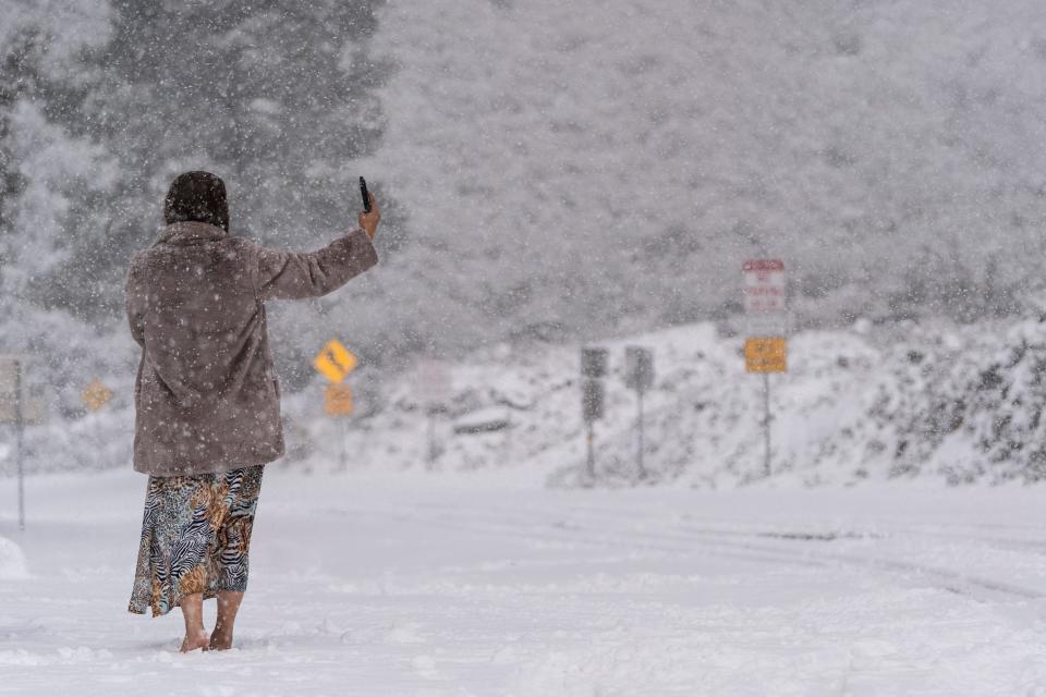 A visitor stands on a snow-covered road while taking a selfie in the Angeles National Forest near La Canada Flintridge, Calif., Thursday, Feb. 23, 2023.