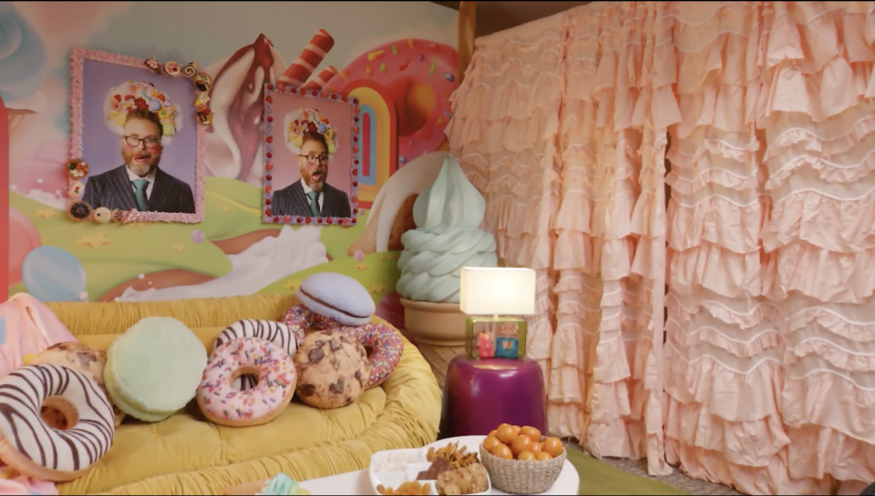 An image of the couch and curtains that make up the set of Rekha Shankar's room in the 'Game Changer' finale, "The Ratfish." Two pictures of Sam Reich making funny poses hang on the wall. 