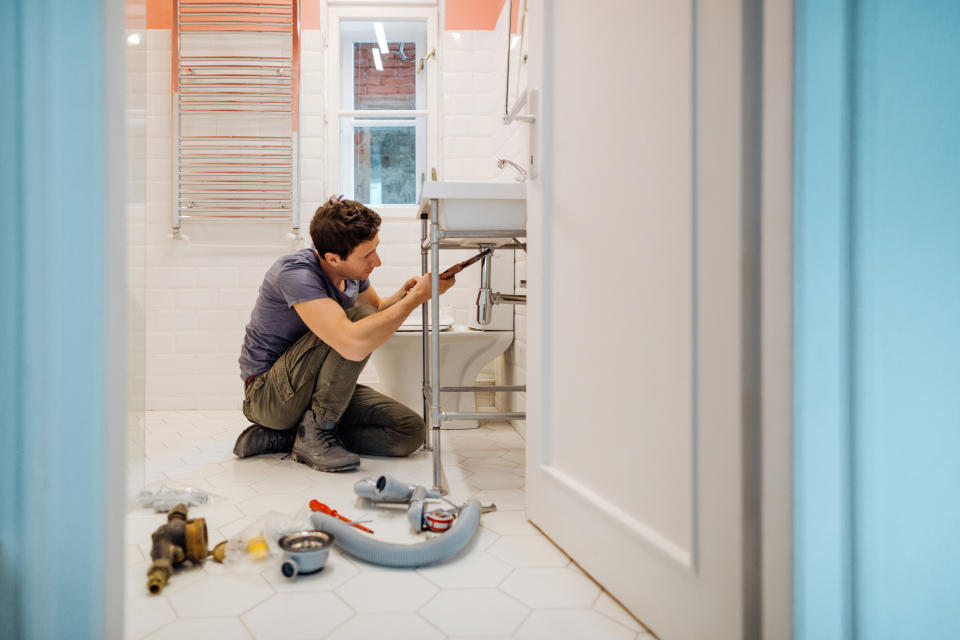 Person repairing sink pipes in bathroom, tools scattered around on floor