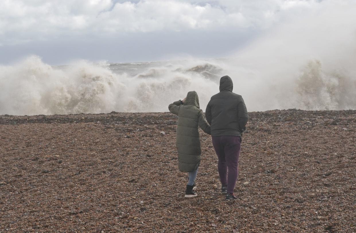 Two people walk on a beach in Dover as huge waves crash ashore (PA)