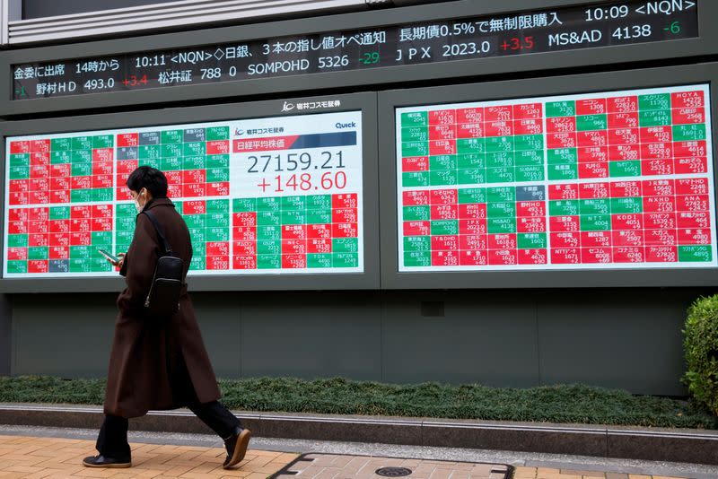 FILE PHOTO: Man walks past an electronic board showing Japan's Nikkei average and stock prices outside a brokerage, in Tokyo