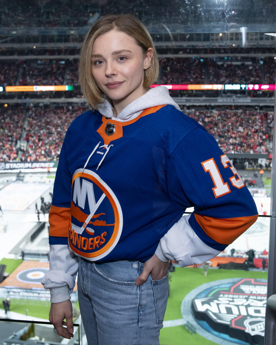 Chloë Grace Moretz wearing an NY Islanders jersey standing in front of a hockey rink