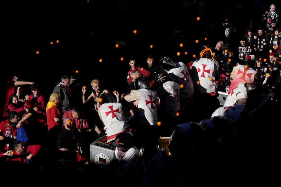 People wearing protection helmets and costumes pelt each other with oranges during the 'Battle of the Oranges" part of Carnival celebrations in the northern Italian Piedmont town of Ivrea, Italy, Tuesday, Feb. 13, 2024. (AP Photo/Antonio Calanni)