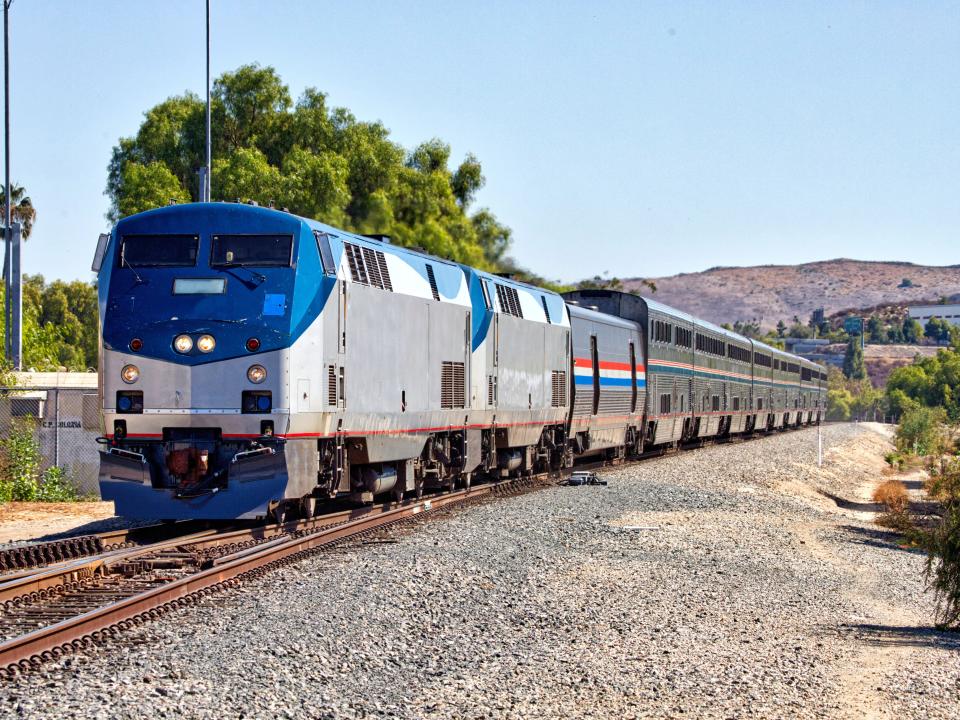 An Amtrak train on a set of rails in a rural landscape.